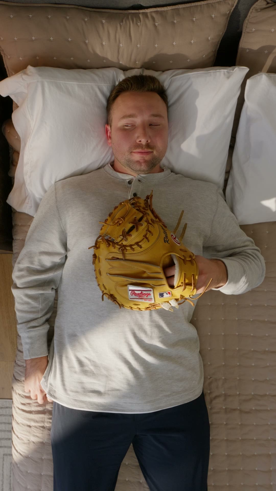 Cal Raleigh lying in bed with the catcher's mitt on his chest, the opening frame of the Reel